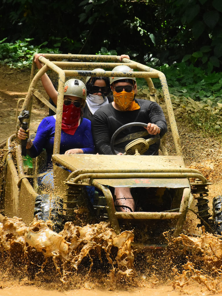 A group of people driving all-terrain buggies through a muddy road.